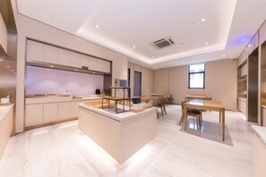 A modern kitchen with a central island, dining area with tables, and a large window providing natural light.