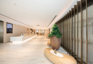 A modern hotel lobby with a reception desk, seating area, and a large potted plant.