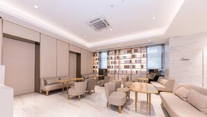 A modern hotel lobby with sofas, tables, and a large bookshelf. - Ji Hotel (Shanghai)