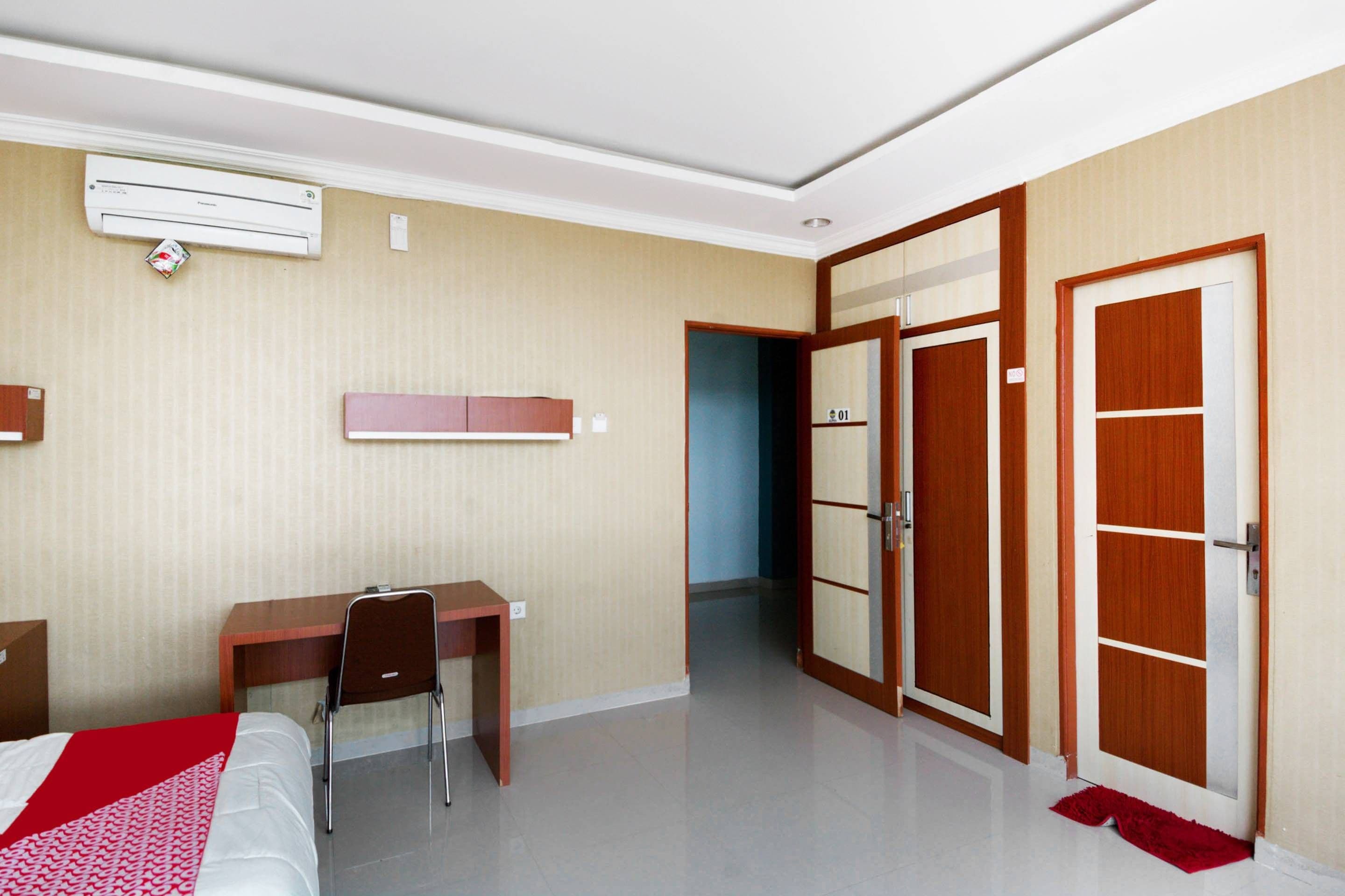 A hotel room with a bed, desk, chair, wardrobe, and an air conditioning unit.