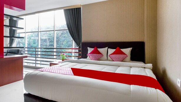 A hotel room with a large bed, a desk, a chair, and a window with curtains. - Super OYO 3431 Alpha Hotel Syariah (Palembang)