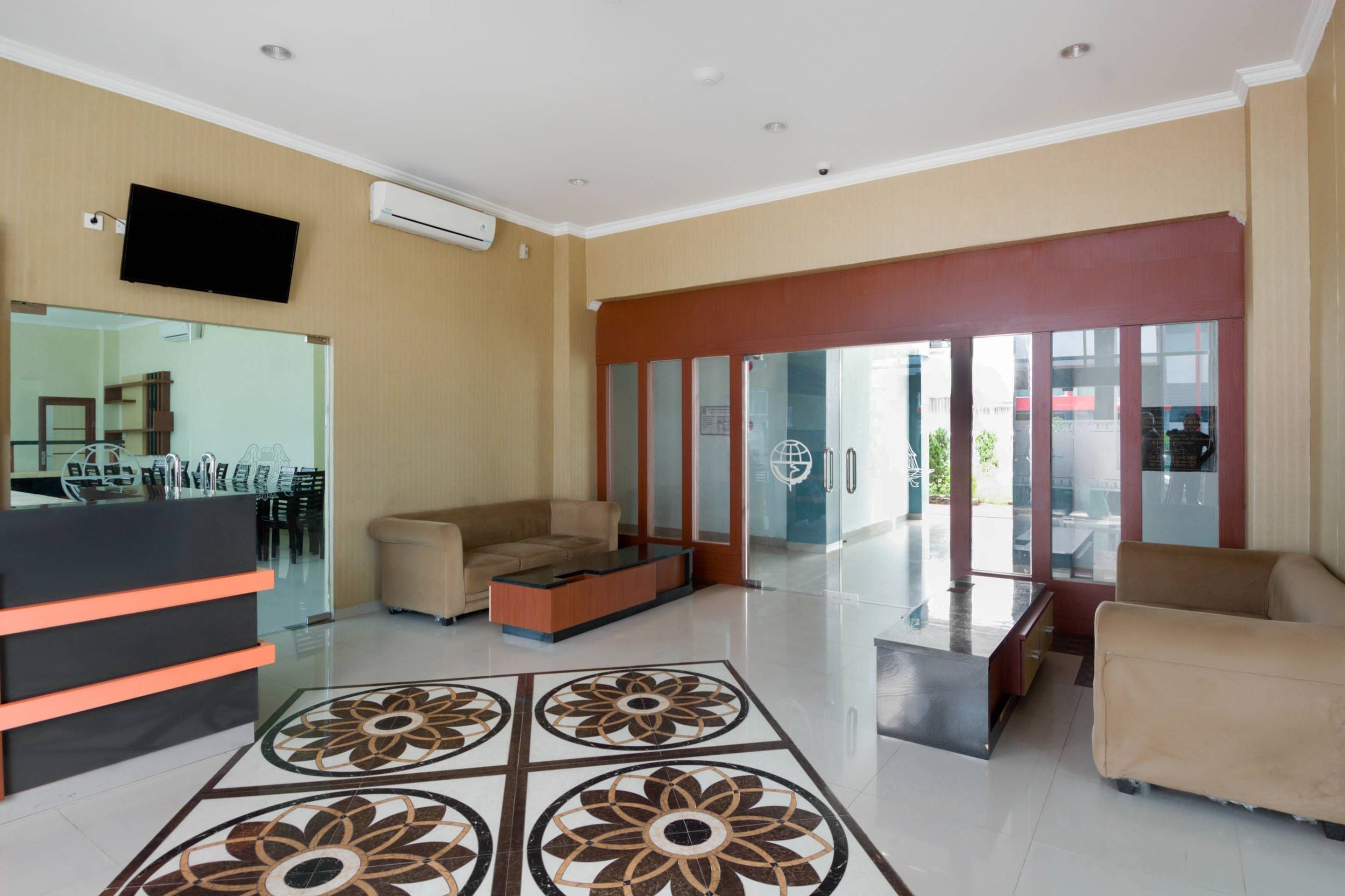 A hotel lobby with a reception desk, seating area, and a large glass door leading outside.