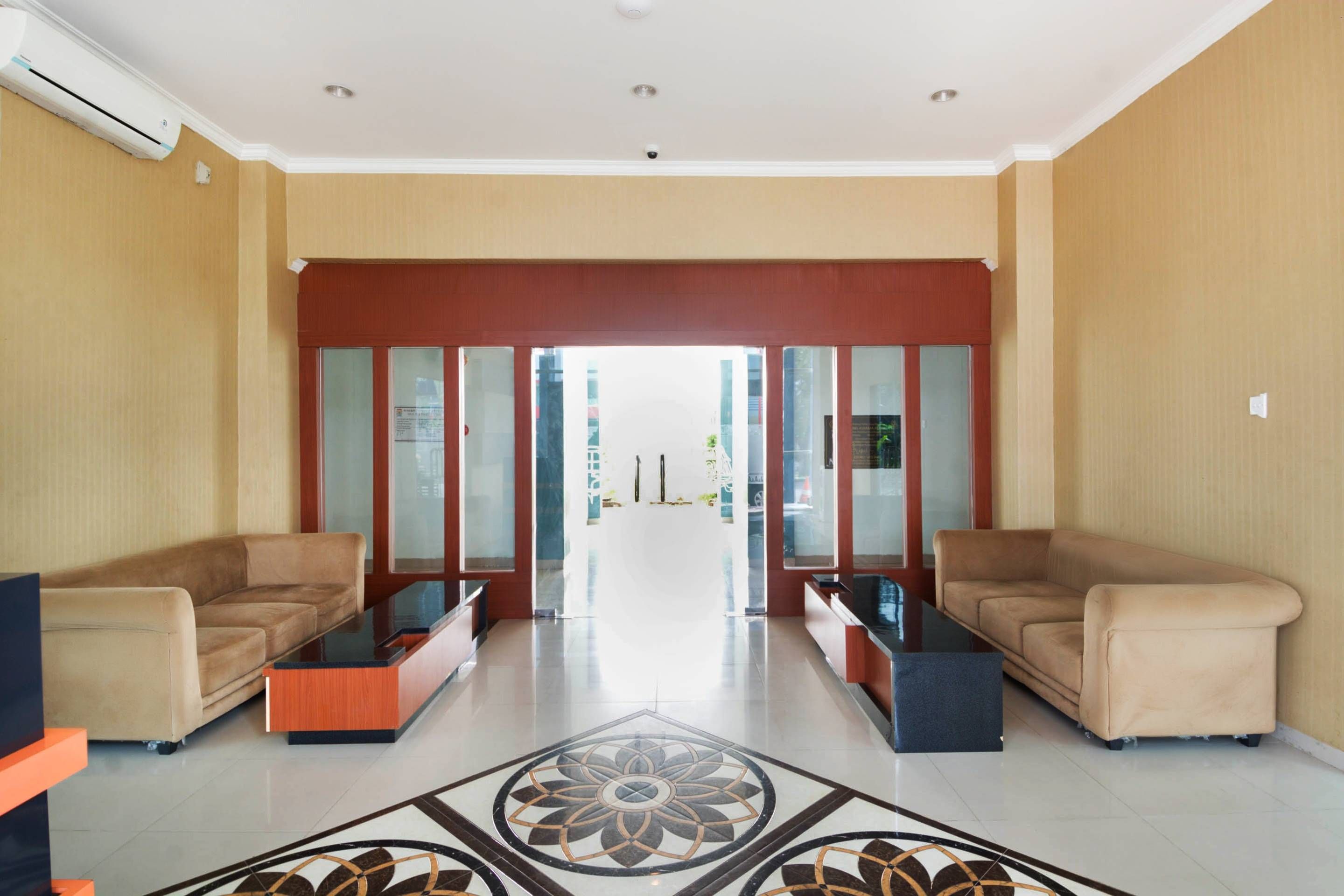 A hotel lobby with a reception desk, two sofas, a patterned floor, and a view through the glass doors.