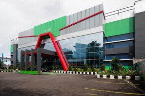 A modern building with a green and red facade, large glass windows, and a prominent red archway. - Super OYO 3431 Alpha Hotel Syariah (Palembang)