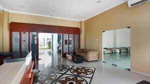 A lobby with a reception desk, a sofa, a patterned floor, and a glass door leading outside. - Super OYO 3431 Alpha Hotel Syariah (Palembang)