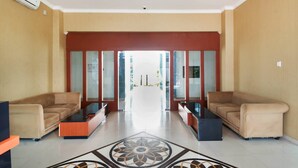 A hotel lobby with a reception desk, two sofas, a patterned floor, and a view through the glass doors. - Super OYO 3431 Alpha Hotel Syariah (Palembang)