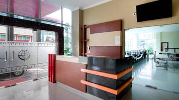 A reception desk with a modern design, a flat-screen TV mounted on the wall, and a glass door leading outside.