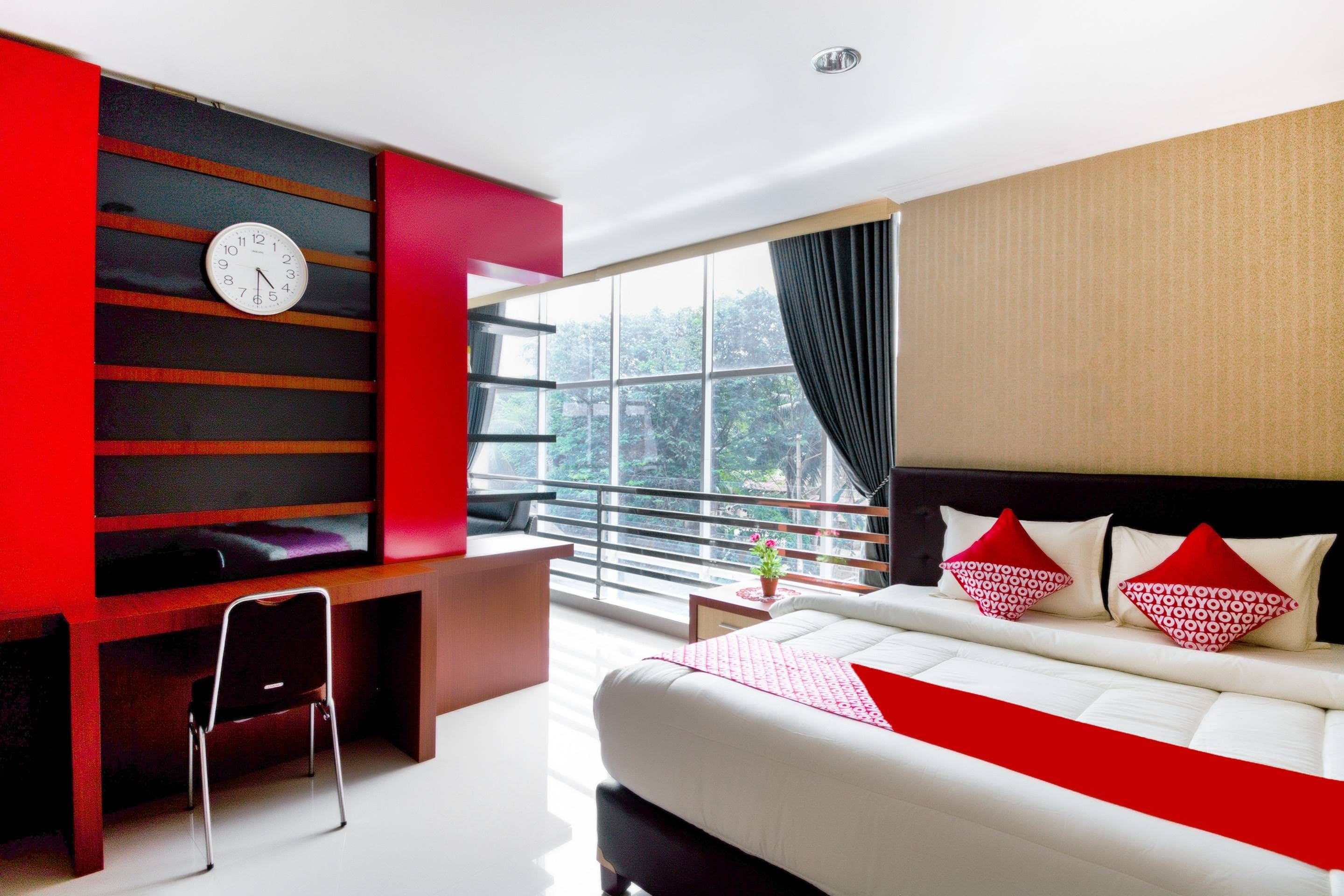 A modern hotel room with a bed, a desk, a chair, a TV, and a large window.
