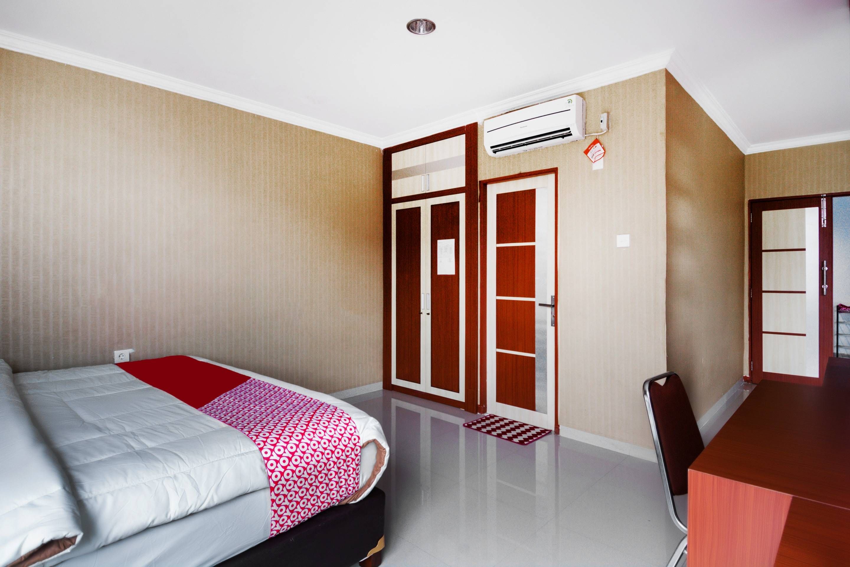 A hotel room with a bed, a desk, a wardrobe, and an air conditioning unit.