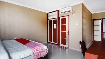 A hotel room with a bed, a desk, a wardrobe, and an air conditioning unit.