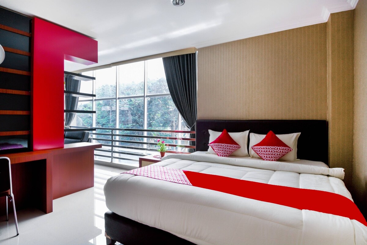 A modern hotel room with a large bed, a desk, and a balcony with a view.