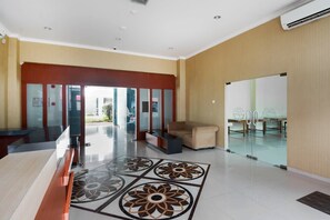 A lobby with a reception desk, a sofa, a patterned floor, and a glass door leading outside. - Super OYO 3431 Alpha Hotel Syariah (Palembang)