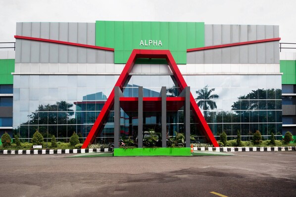 A modern building with the word 'ALPHA' on the facade, large glass windows, and a green and red architectural feature.