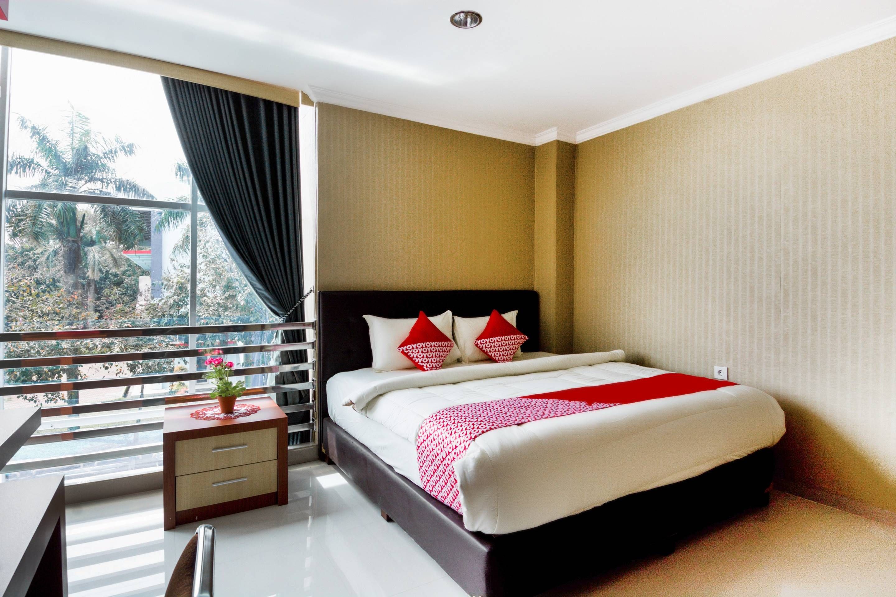 A hotel room with a bed, a desk, and a window with a view of trees.