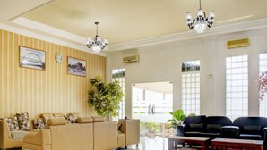 A spacious lobby with a beige sofa set, a black sofa, and a wooden coffee table. There are two large windows and a chandelier. - Capital O 90395 Hotel Nascar Family (Palangkaraya)