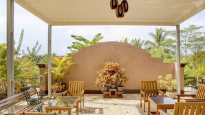 A covered outdoor seating area with wooden furniture and potted plants, surrounded by palm trees and a view of the sky. - Capital O 90395 Hotel Nascar Family (Palangkaraya)