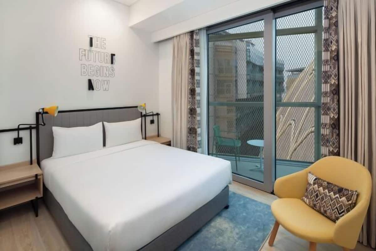 Moderni hotellihuone, jossa on suuri sänky, pieni työpöytä, tuoli ja liukuovi, joka johtaa parvekkeelle.
