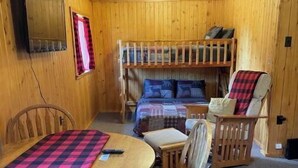 A cozy cabin interior with a bunk bed, a dining table with chairs, and a television mounted on the wall. - Ursa Miner - quiet, dark sky, 6 miles from Pitkin! (Parlin)
