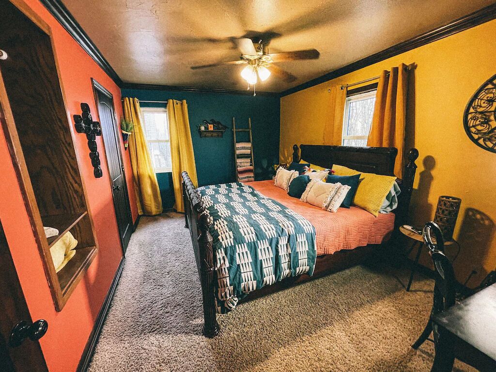 A bedroom with a bed, a ceiling fan, a window with curtains, and a wall decoration.