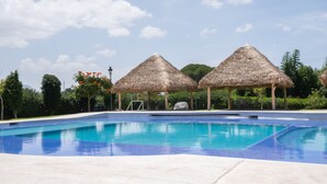 Una piscina con estructuras de techo de paja, rodeada de vegetación.