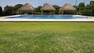 Una piscina con tres estructuras de techo de paja al fondo.