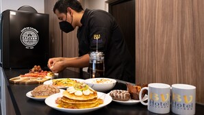 A hotel kitchen with a chef preparing food, various dishes on the counter, and branded coffee mugs. - BV Hotel Atlixco (Atlixco)