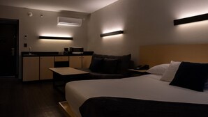 A compact hotel room with a bed, a small desk, a kitchenette, and a built-in air conditioning unit. - BV Hotel Atlixco (Atlixco)