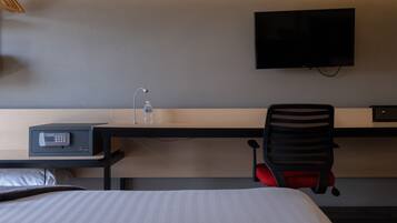 Habitación de hotel con cama, escritorio con computadora, una silla, televisor montado en la pared y minibar.