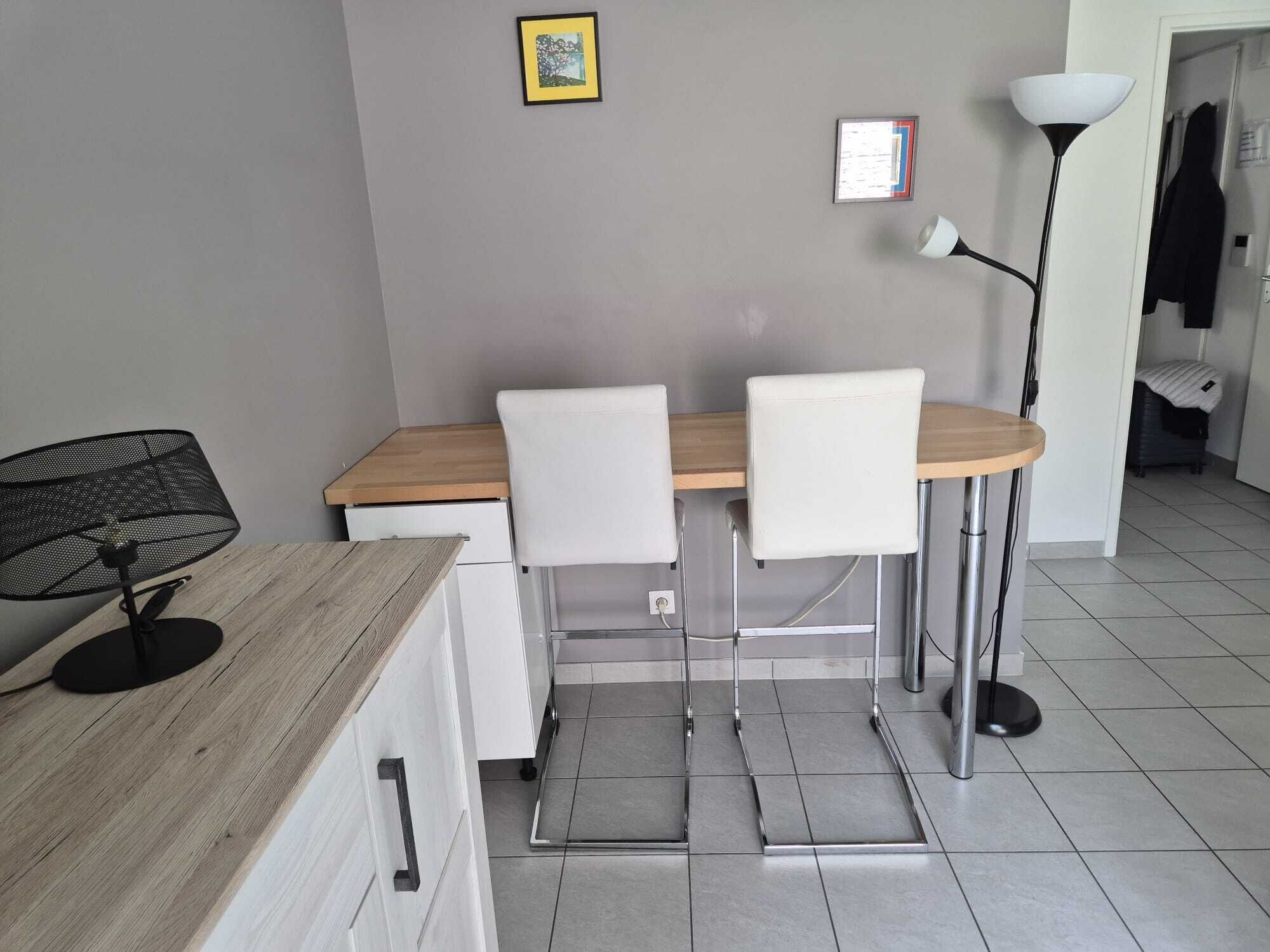A small dining area with a wooden table, two white chairs, a black mesh chair, and a floor lamp.