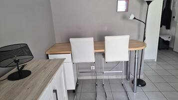 A small dining area with a wooden table, two white chairs, a black mesh chair, and a floor lamp.