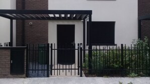 A modern two-story building with a white facade, a black gate, and a small covered patio area. - Hortillonne (AMIENS)