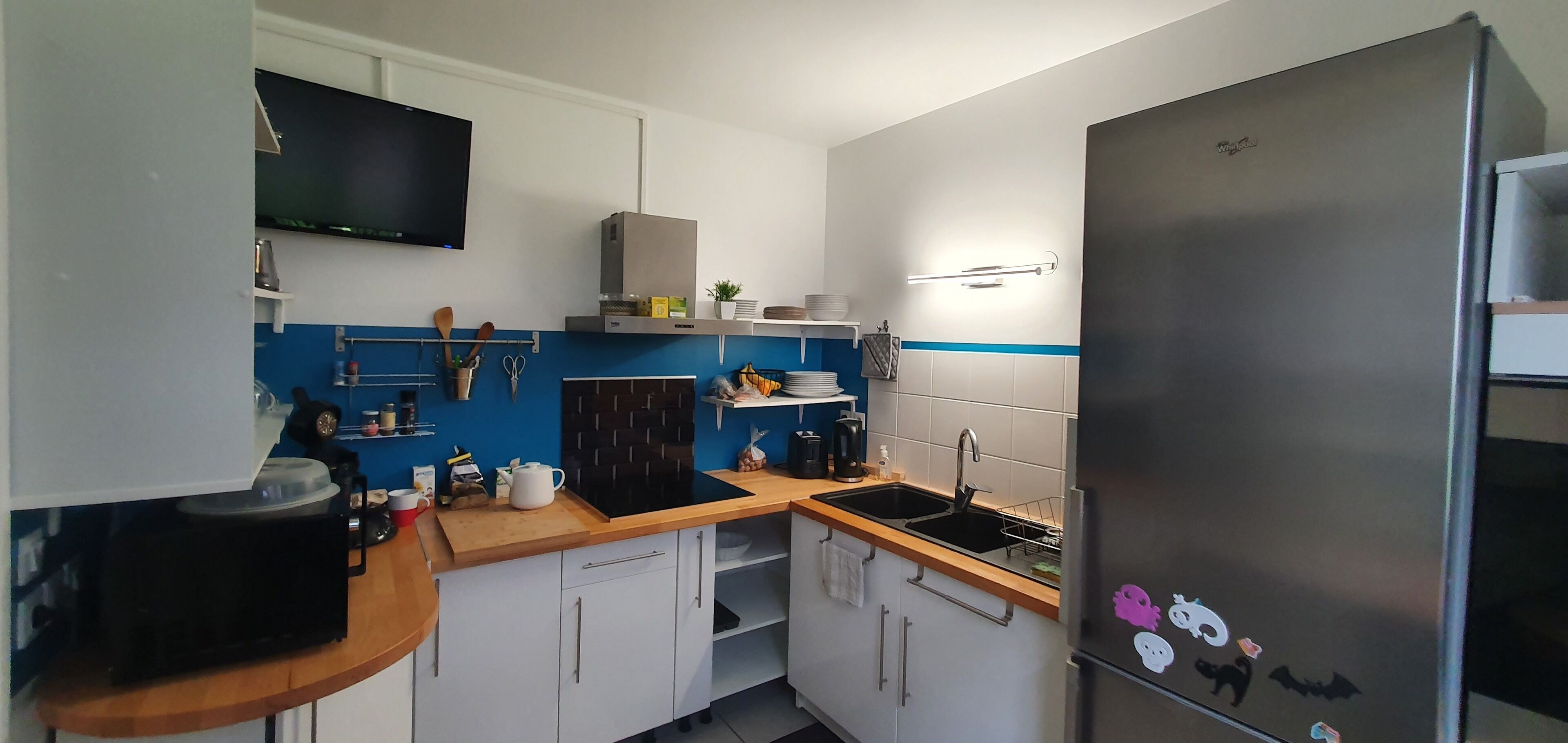 Una cocina compacta con armarios blancos, un refrigerador negro y un protector contra salpicaduras azul.
