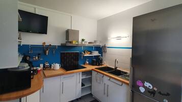 Una cocina compacta con armarios blancos, un refrigerador negro y un protector contra salpicaduras azul.