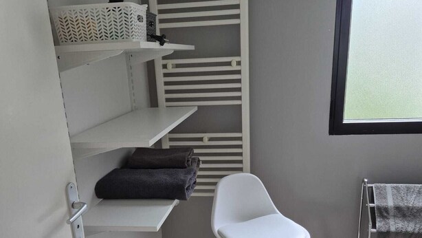 A small, modern bathroom with white shelves, a white chair, and a towel rack. - Hortillonne (AMIENS)
