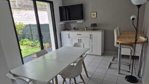 A modern kitchen with a flat-screen TV, a dining table with chairs, and a small cabinet. - Hortillonne (AMIENS)