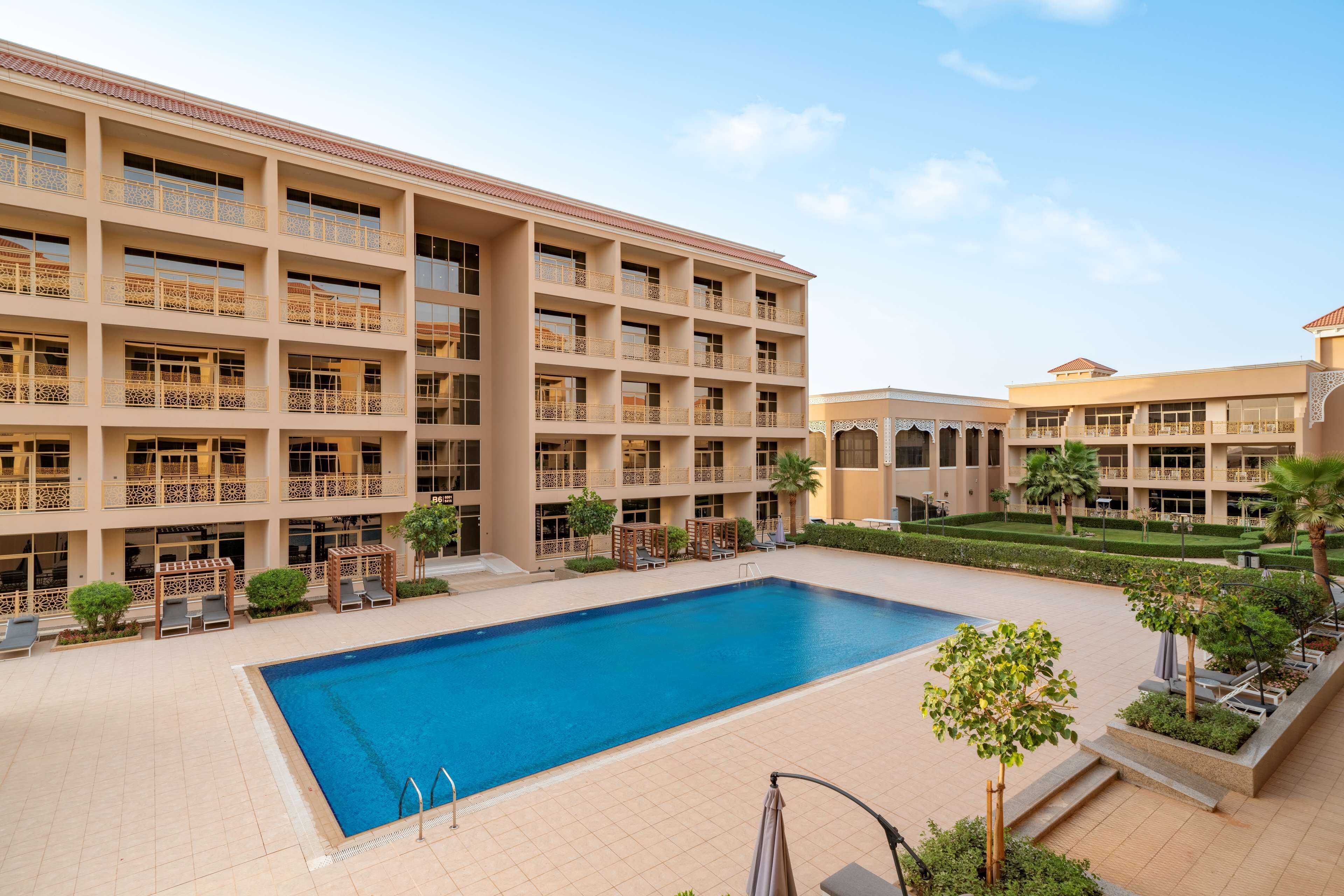 A multi-story hotel with a swimming pool, outdoor seating, and a well-maintained garden.