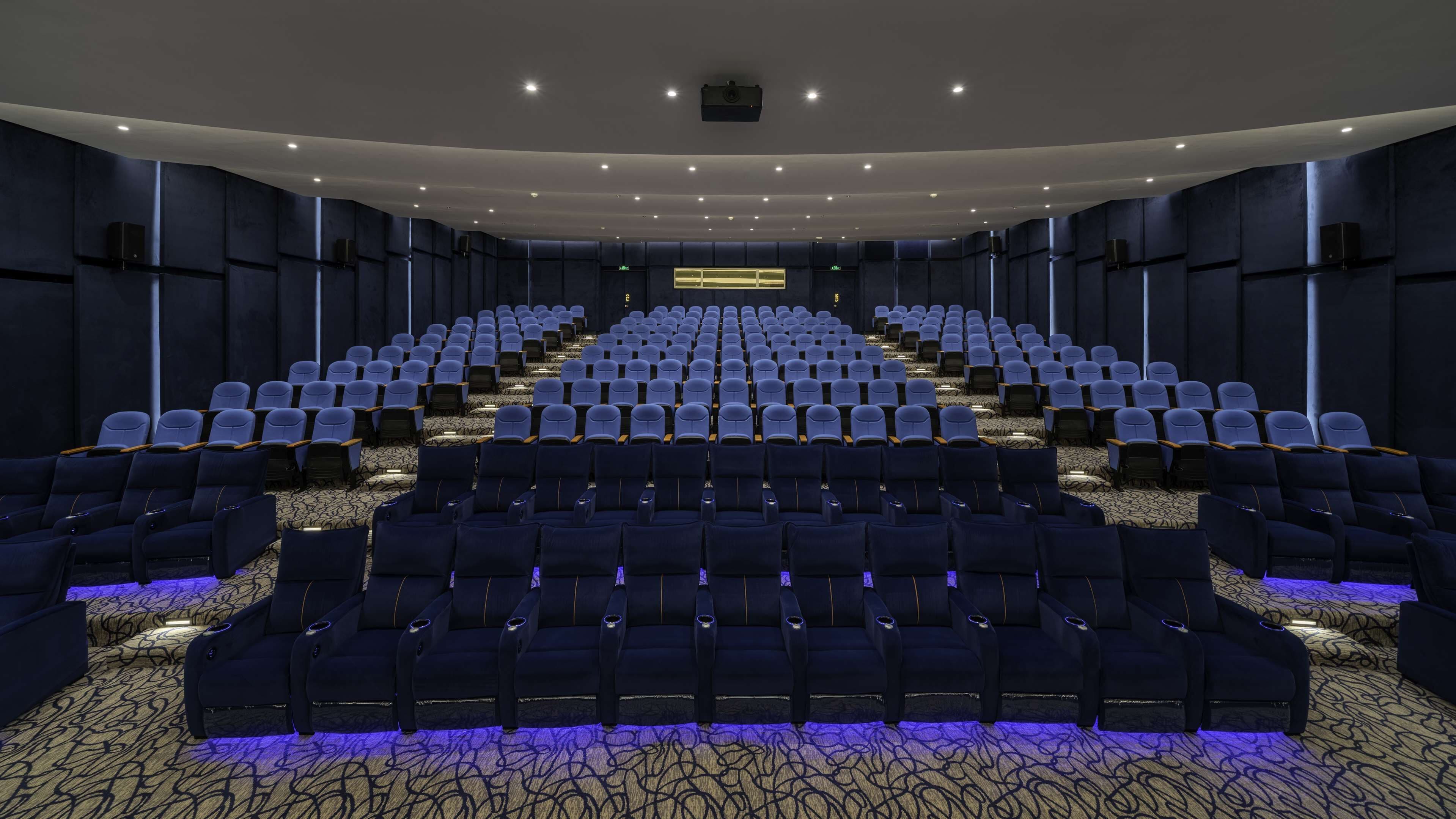 Un teatro con hileras de asientos, un escenario frontal y suelo alfombrado.