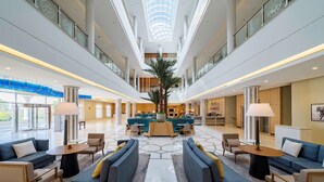 Un vestíbulo amplio con una zona de estar central, una palmera grande y un diseño moderno.