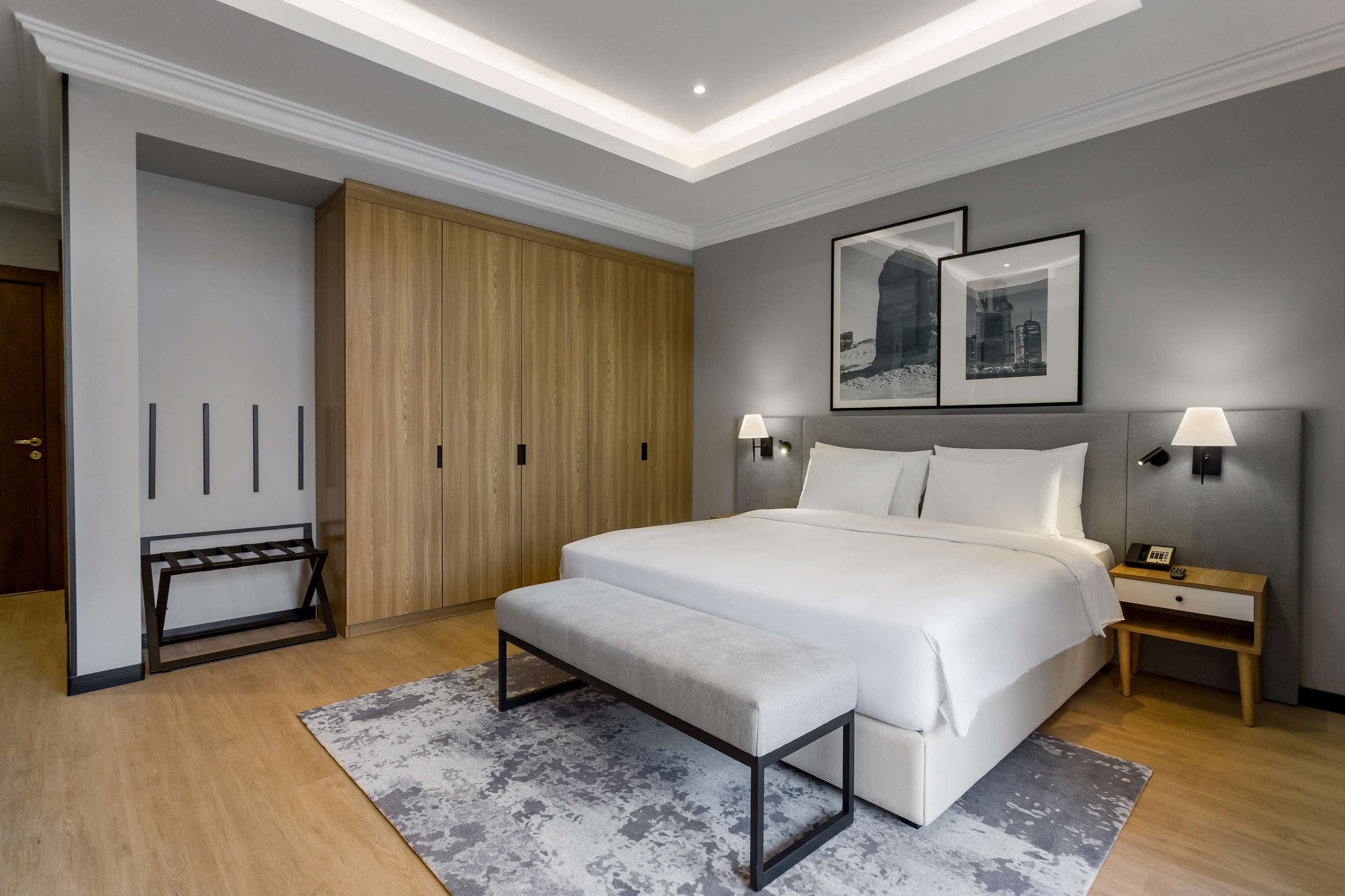 A modern bedroom with a large bed, bedside tables, a bench, and a wardrobe.