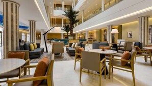 Un lobby amplio con varias zonas de estar, una palmera central y un techo alto con tragaluces.