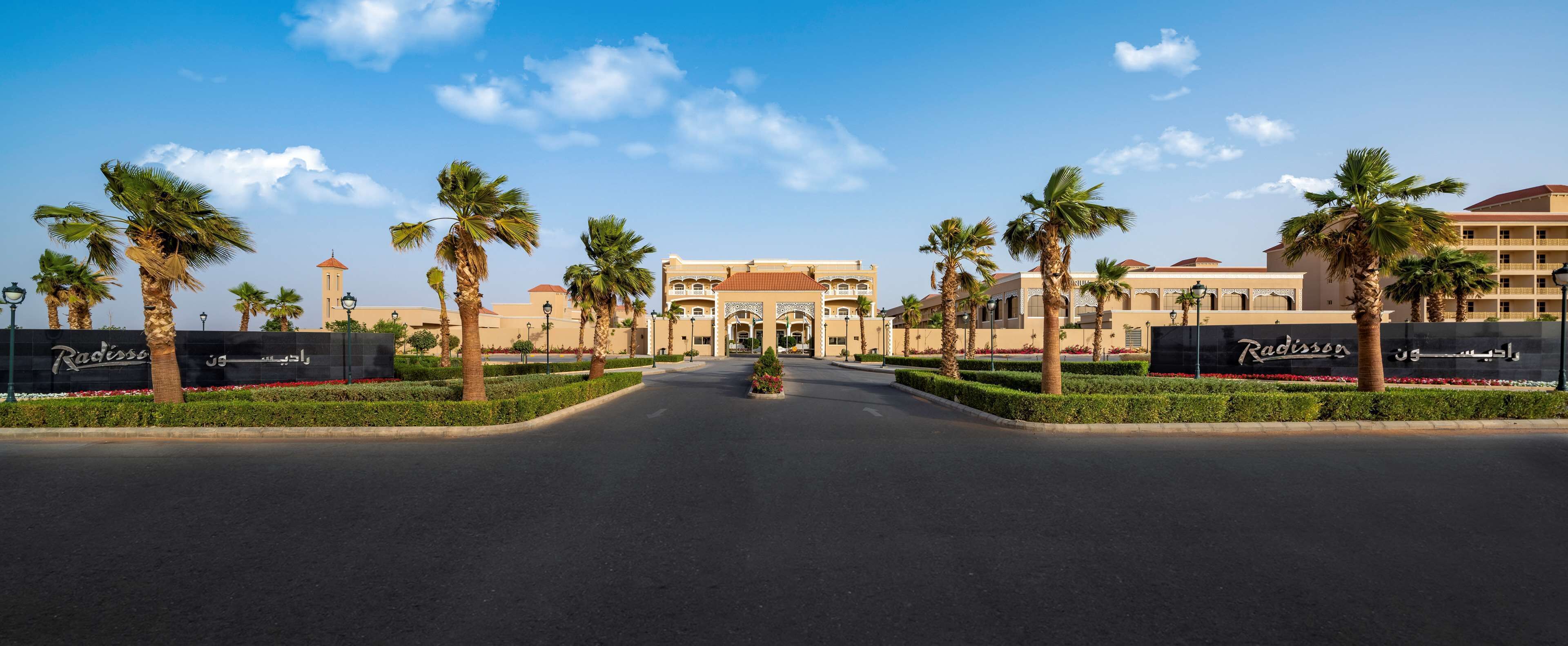 A hotel entrance with a central archway, palm trees, and a clear sky.