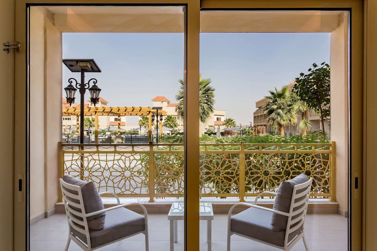 A balcony with two white chairs and a small table, a decorative yellow fence, and a view of buildings and palm trees.