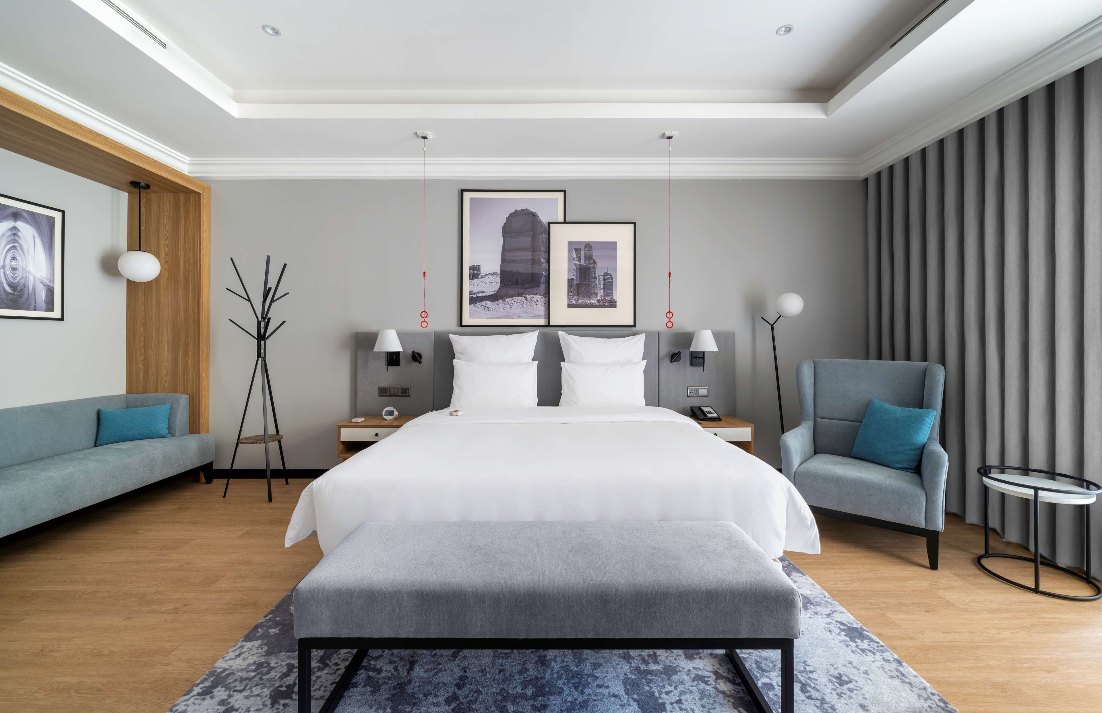 A modern hotel room with a large bed, a grey sofa, a small round table, and a chair.