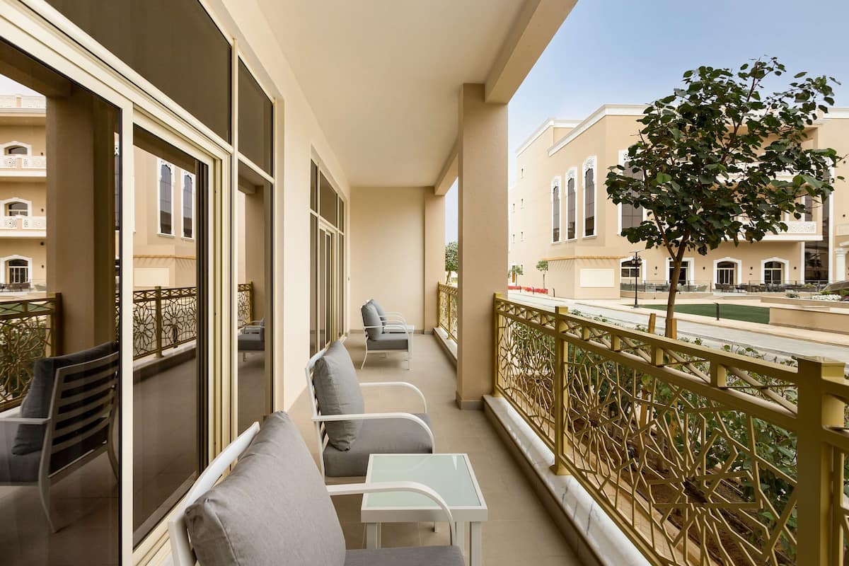 A balcony with seating, a view of buildings, and a tree.