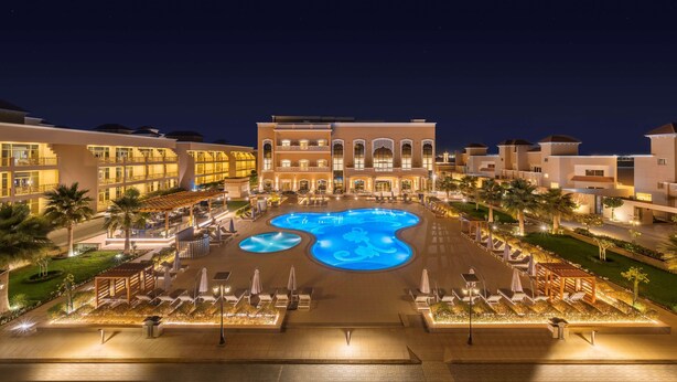 Un hotel con una amplia piscina central, varios balcones y un área exterior bien iluminada.
