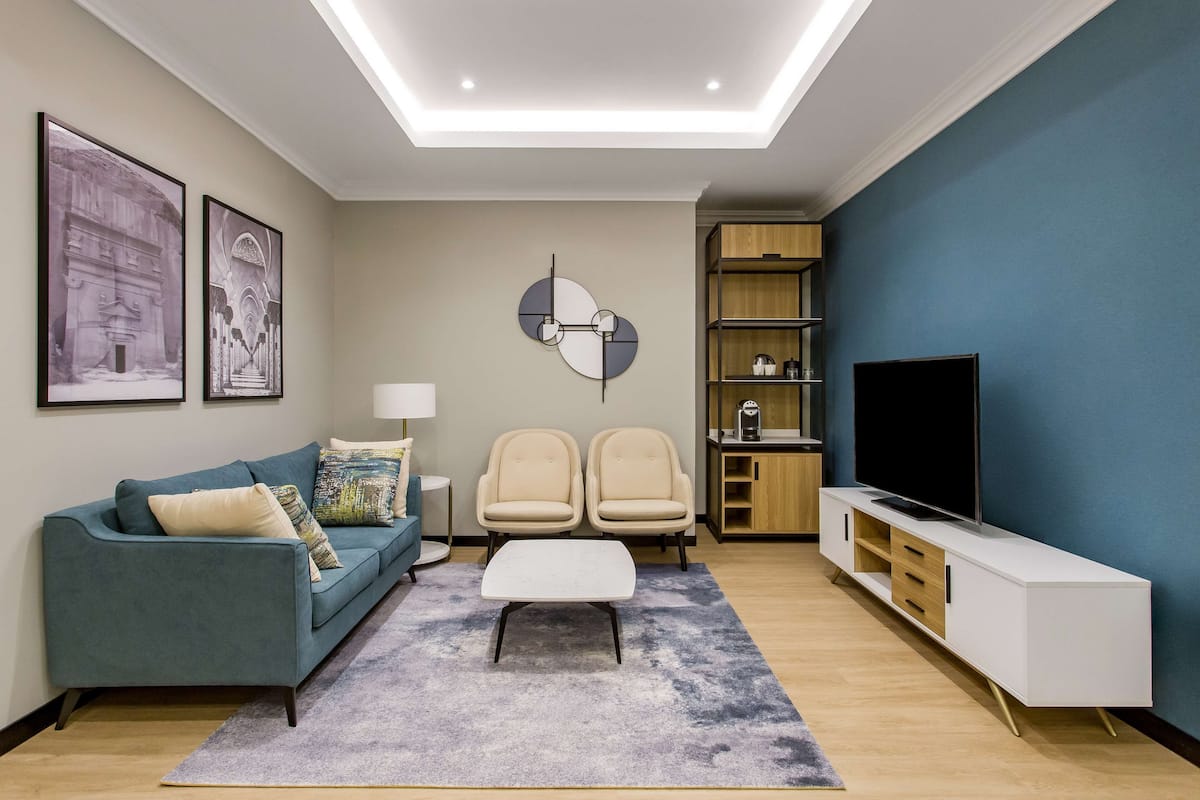 A modern living room with a sofa, two chairs, a coffee table, a TV, and a bookshelf.