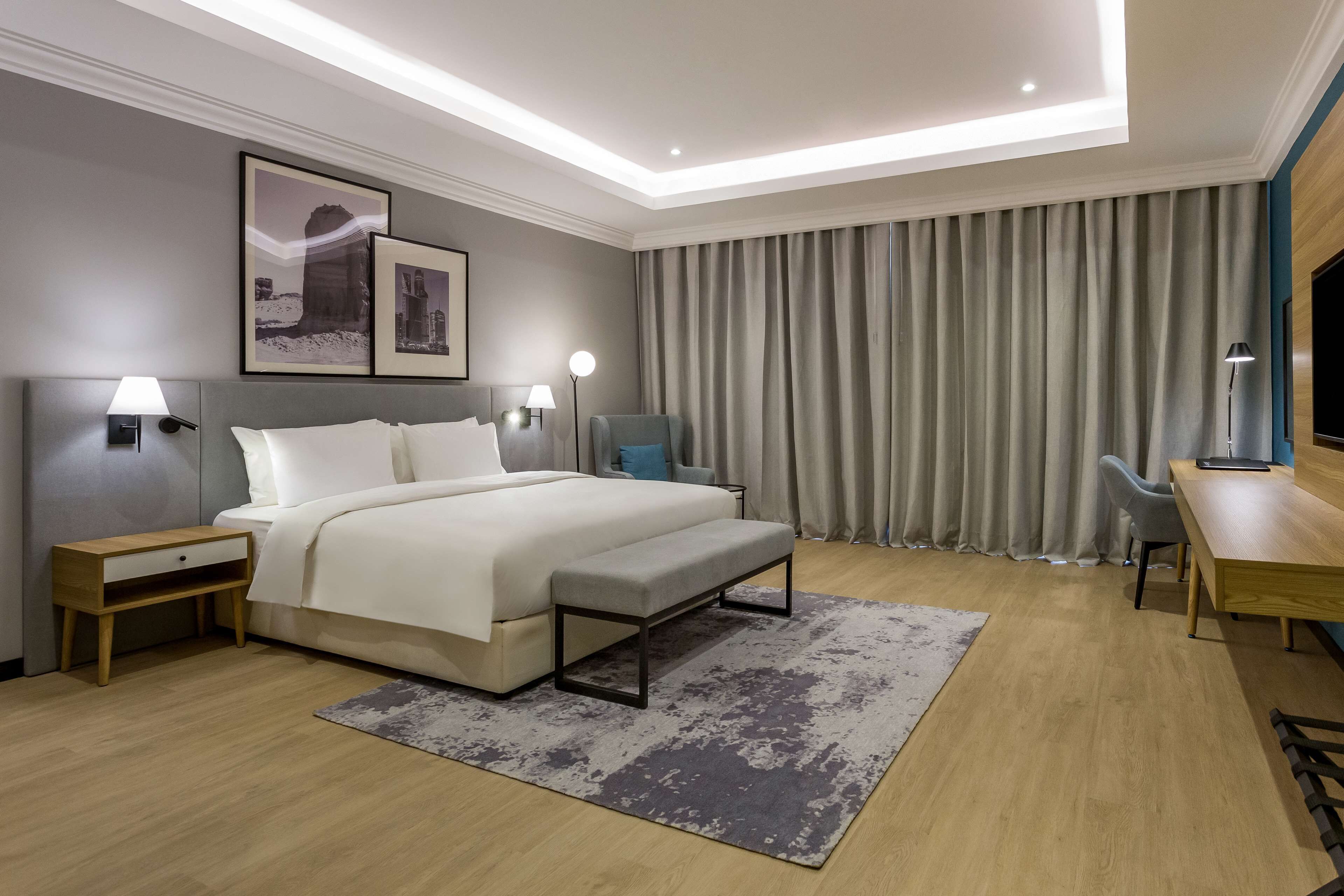 Ein modernes Hotelzimmer mit einem großen Bett, Nachttischen, einem Schreibtisch und einem Fernseher.