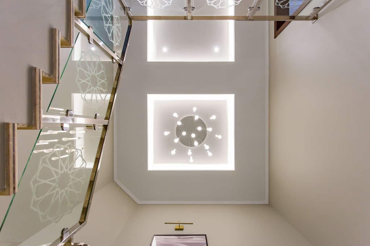 A modern interior with a staircase, glass railings, and recessed ceiling lighting.