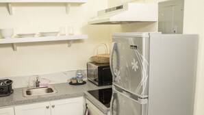 Una cocina con armarios blancos, un refrigerador de acero inoxidable, un microondas y un lavamanos.