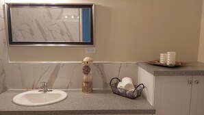 Un baño con lavamanos de mármol, un espejo, un perchero para toallas, una cesta con toallas y una bandeja con velas.
